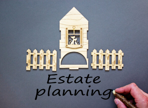 Hand writing 'estate planning' on grey background. Model of a wooden house. Male hand, wooden fence. Copy space. Business concept.